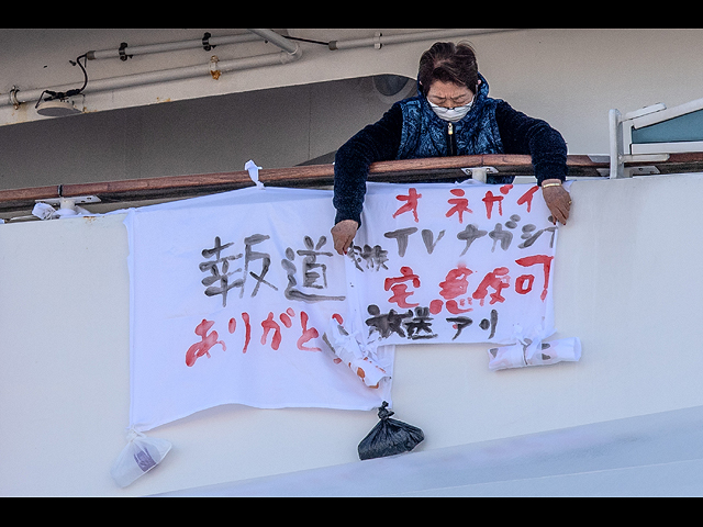 Пассажир вешает баннер с надписью "Спасибо, что сообщили об этом", слева от которого баннер с надписью "Пожалуйста, передайте это по телевизору" на круизном лайнере Diamond Princess. 10 февраля 2020 года, Иокогама, Япония
