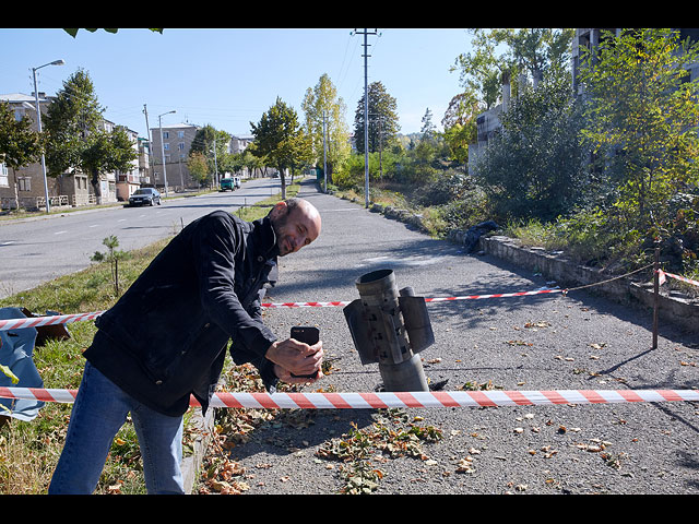 Житель позирует рядом с неразорвавшейся ракетой на улице города. Шуши, Нагорный Карабах, 12 октября 2020 года