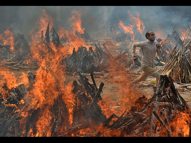 Мужчина бежит, спасаясь от жары погребальных костров жертв COVID-19. Индия, Дели.