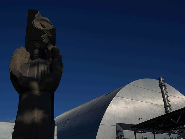 Монумент ликвидаторам рядом с новым защитным сооружением, закрывающим взорвавшийся реактор на Чернобыльской атомной электростанции. 2026 год 