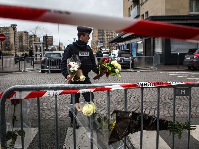Полицейский несет переданные прохожими цветы на место теракта в магазине "Гипер Кошер". Париж, 10.01.2015