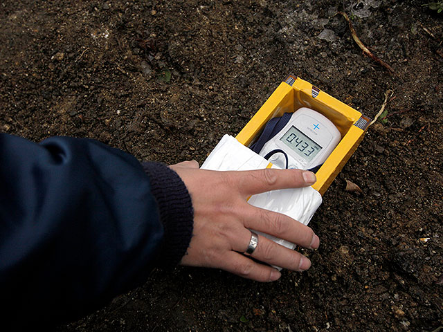 Рабочий проверяет уровень радиации у верхнего слоя почвы у частного дома в Фукусиме. 21 февраля 2012 года