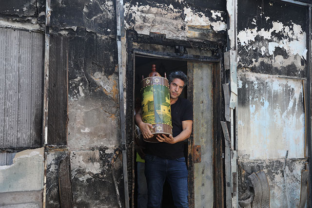 Израильтянин выносит свитки Торы из сожженной синагоги после ночных беспорядков. Лод, 12 мая 2021 года