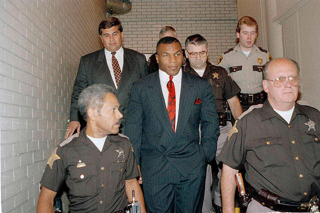 Майка Тайсона (в центре) сопровождают полицейские после предъявления обвинения в изнасиловании.1991 год