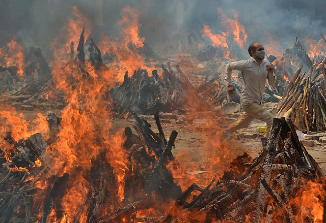 Мужчина бежит, спасаясь от жары погребальных костров жертв COVID-19. Индия, Дели.