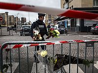 Полицейский несет переданные прохожими цветы на место теракта в магазине 